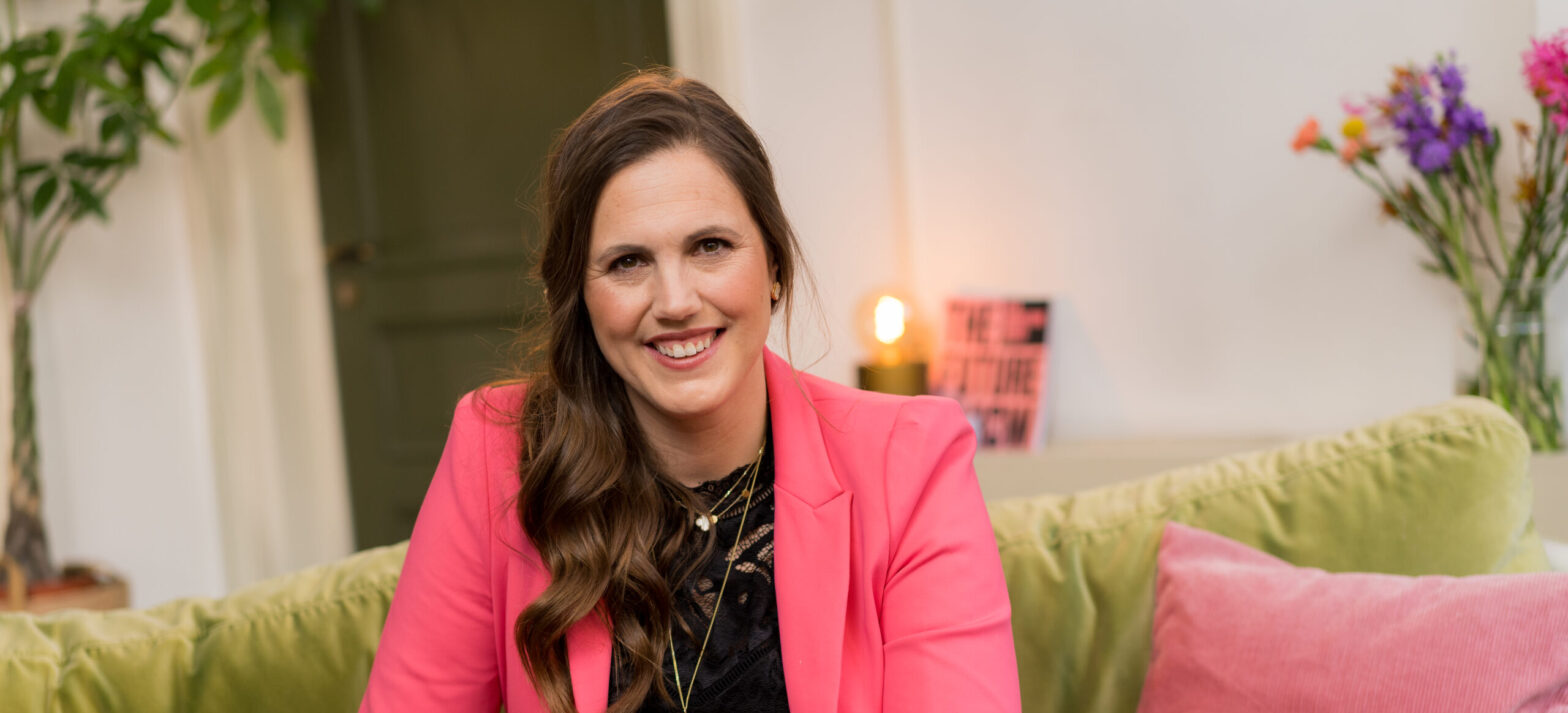 Marieke sitting on a green sofa, wearing a pink blazer