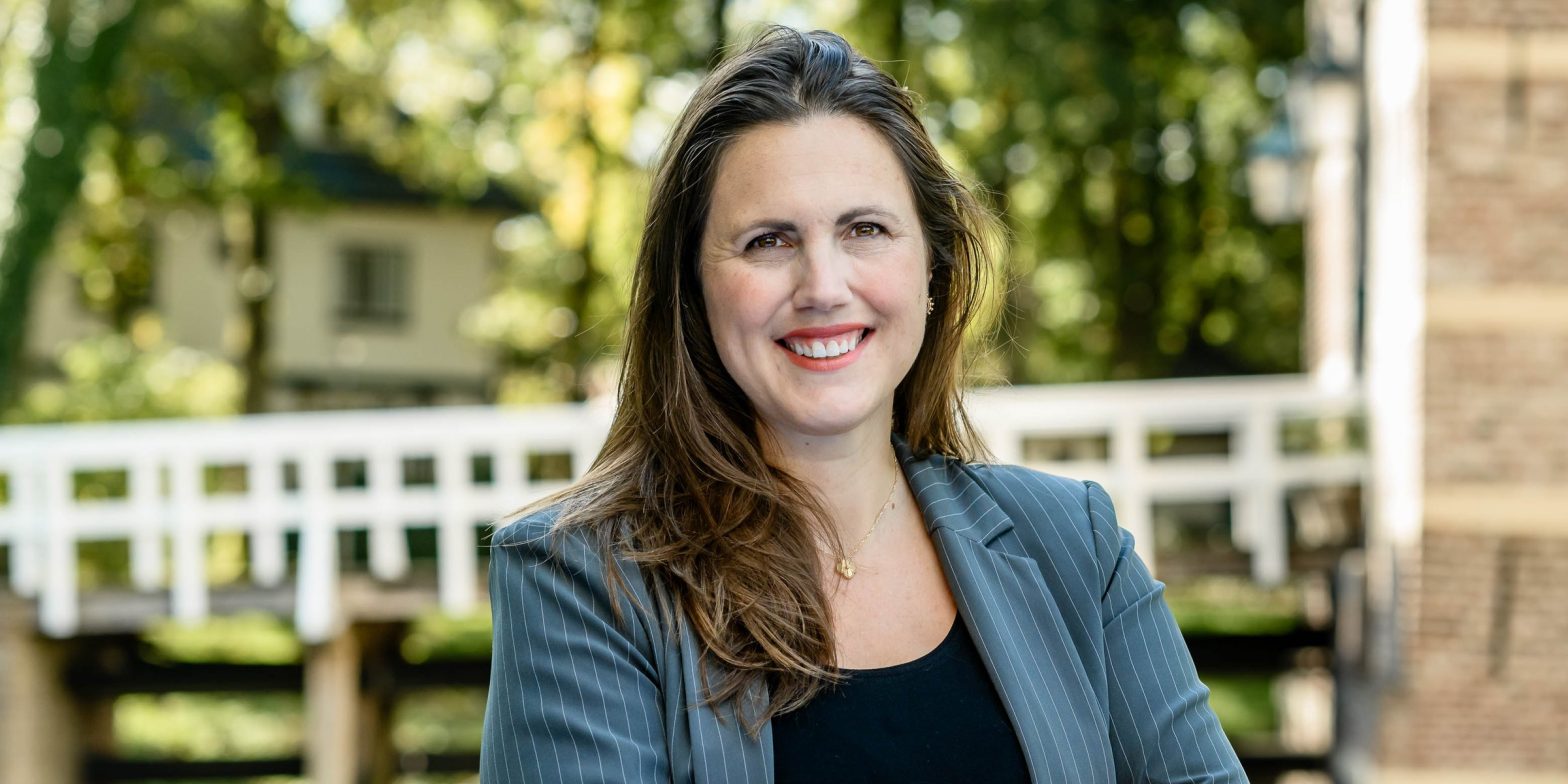 Marieke van de Rakt, smiling, in a grey pinstripe blazer outdoors